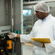 Male worker holding clipboard while operating machine in juice factory